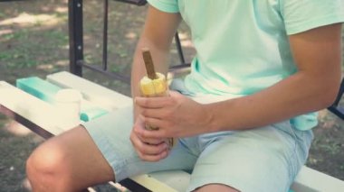 ereksiyon taklit alt karın park ve açık hotdog ambalaj bir bankta oturmuş, bir hotdog tutan genç bir yalnız adam. 4k, ağır çekim