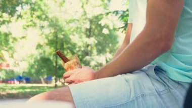 ereksiyon taklit alt karın park ve açık hotdog ambalaj bir bankta oturmuş, bir hotdog tutan genç bir yalnız adam. 4k, ağır çekim