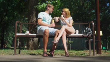 Mutlu çifti eğleniyor bir bankta bir şehir parkta sosisli yeme. 4k, ağır çekim.