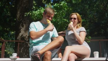 Mutlu çifti eğleniyor bir bankta bir şehir parkta sosisli yeme. 4k, ağır çekim.