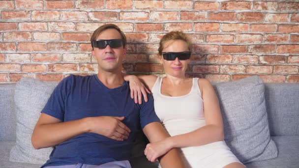 Fecha. um jovem casal em óculos 3d, sentado no sofá na sala de estar com muitas emoções, assistir o filme. 4k, câmera lenta . — Vídeo de Stock