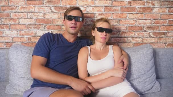 Z bliska. Młoda para w okulary 3d, siedząc na kanapie w salonie z wielu emocji, obejrzeć film. 4k, zwolnionym tempie. — Wideo stockowe