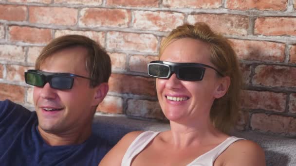 Закрывай. молодая пара в очках 3d, сидя на диване в гостиной со многими эмоциями, смотреть фильм. 4k, slow motion . — стоковое видео