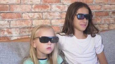 Kapatın. iki küçük kız bardaklarda 3d, film izlerken çok duygu ile oturma odasında kanepede oturuyor. 4k, ağır çekim.