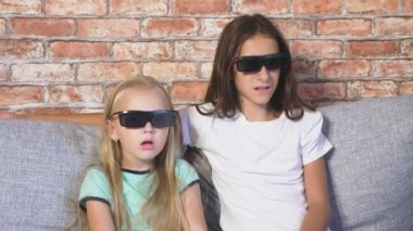 Kapatın. iki küçük kız bardaklarda 3d, film izlerken çok duygu ile oturma odasında kanepede oturuyor. 4k, ağır çekim.