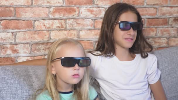 Cerca. dos niñas en gafas 3d, sentadas en el sofá en la sala de estar con muchas emociones, viendo la película. 4k, cámara lenta . — Vídeos de Stock