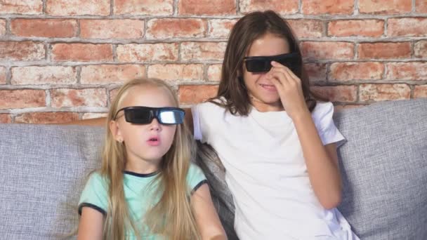 Schließen. zwei kleine Mädchen in Brille 3D, die mit vielen Emotionen auf der Couch im Wohnzimmer sitzen und sich den Film ansehen. 4k, Zeitlupe. — Stockvideo