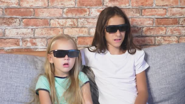 Κλείστε. δύο μικρά κορίτσια στα γυαλιά 3d, κάθεται στον καναπέ στο σαλόνι με πολλά συναισθήματα, παρακολουθώντας την ταινία. 4k, αργή κίνηση. — Αρχείο Βίντεο