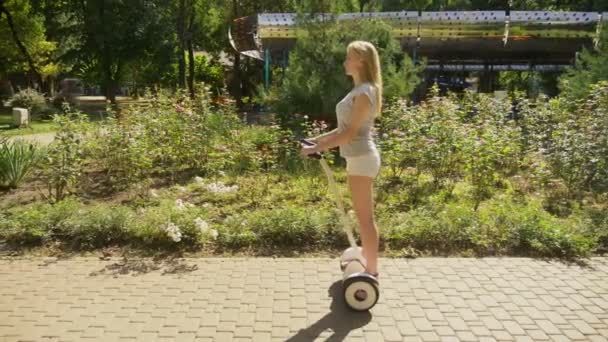 Fille en short blanc, chevauchant un Segway par une journée ensoleillée claire. parc d'été et soleil éblouissant. 4k, tir au ralenti, tir au stadikam — Video