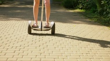 Beyaz şortlu kız açık güneşli bir günde bir Segway sürme. parlama yaz park ve güneş. 4k, ağır çekim silah, stadikam atış