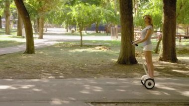 Beyaz şortlu kız açık güneşli bir günde bir Segway sürme. parlama yaz park ve güneş. 4k, ağır çekim silah, stadikam atış