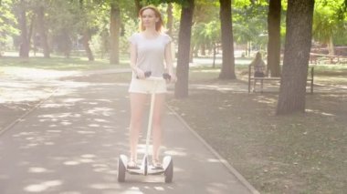 Beyaz şortlu kız açık güneşli bir günde bir Segway sürme. parlama yaz park ve güneş. 4k, ağır çekim silah, stadikam atış