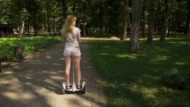 Ragazza in pantaloncini bianchi, cavalcando un Segway in una chiara giornata di sole. parco estivo e bagliore solare. 4k, tiro al rallentatore, stadikam shot — Video Stock