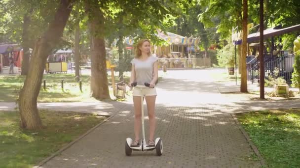 Chica en pantalones cortos blancos, montando un Segway en un día claro y soleado. parque de verano y resplandor solar. 4k, disparo en cámara lenta, disparo en estadikam — Vídeo de stock