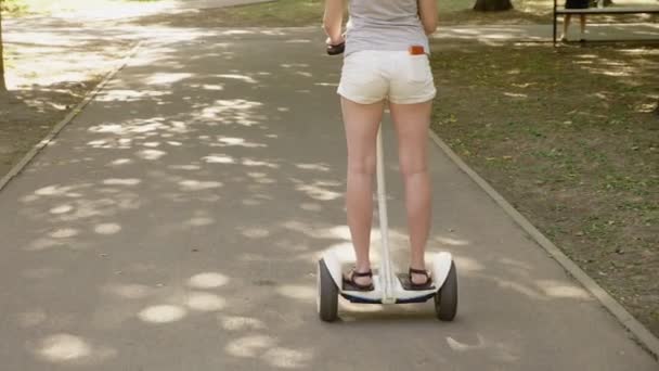 Ragazza in pantaloncini bianchi, cavalcando un Segway in una chiara giornata di sole. parco estivo e bagliore solare. 4k, tiro al rallentatore, stadikam shot — Video Stock