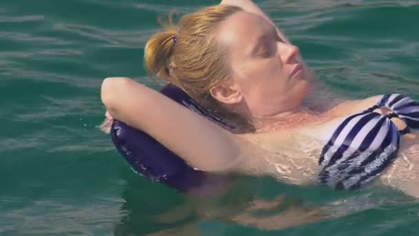 Женщина без грима отдыхает. Девушка плавает в море на спине, лежащей на надувной подушке. 4K замедленной съемки — стоковое видео
