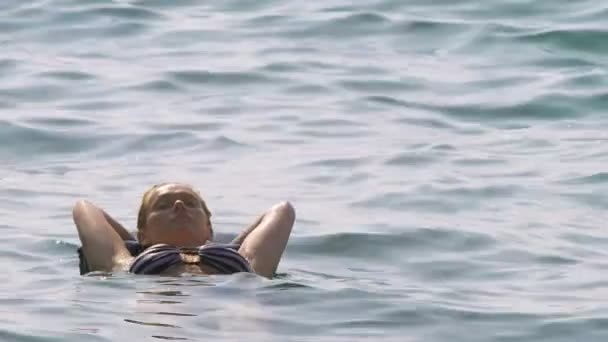 Женщина без грима отдыхает. Девушка плавает в море на спине, лежащей на надувной подушке. 4K замедленной съемки — стоковое видео