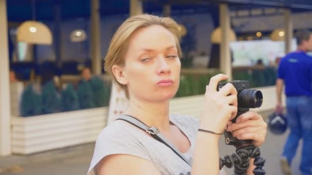 Um fotógrafo profissional, tira fotos em um parque de diversões, uma mulher pressiona um botão de um gadget entre um jardim florido. 4k, câmera lenta, steadicam tiro — Vídeo de Stock
