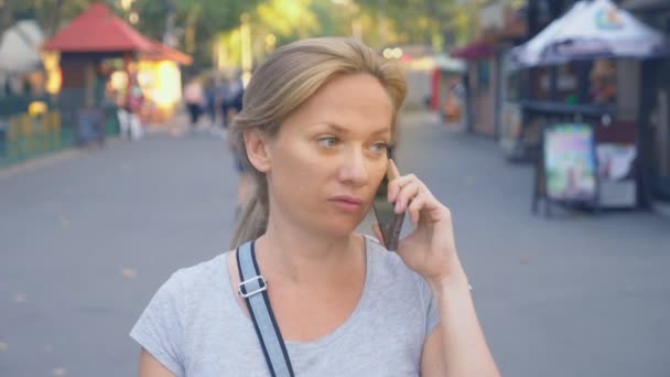 Vrouw gaat naar park met haar telefoon zomerdag onder zonlicht. 4 k, slow-motion, standicam schot — Stockvideo