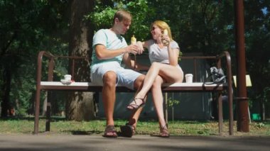 Mutlu çifti eğleniyor bir bankta bir şehir parkta sosisli yeme. 4k, ağır çekim.