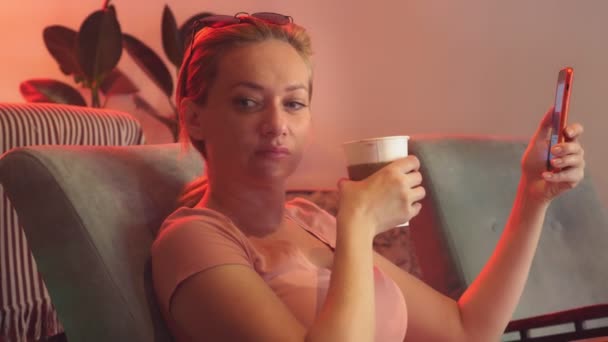 Девушка пьет кофе с печеньем в ретро-кафе и просматривает свой телефон. 4К. Медленное движение — стоковое видео