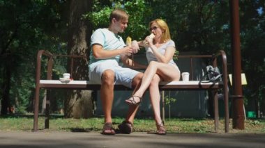 Mutlu çifti eğleniyor bir bankta bir şehir parkta sosisli yeme. 4k, ağır çekim.