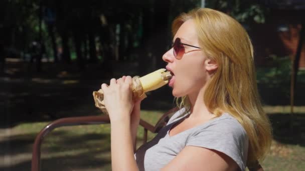 Mädchen Mit Sonnenbrille Würstchen Essen Und Stadtpark Auf Einer Bank — Stockvideo