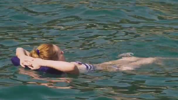 Una mujer sin maquillaje descansando. Una chica está flotando en el mar sobre su espalda acostada sobre una almohada inflable. 4K cámara lenta — Vídeo de stock