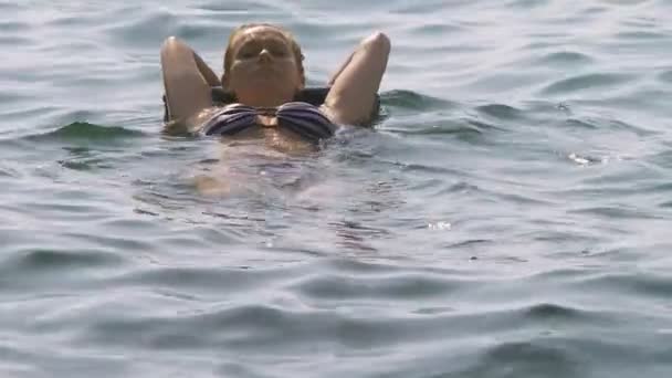 Uma mulher sem maquilhagem a descansar. Uma menina está flutuando no mar em suas costas deitada em um travesseiro inflável. Movimento lento 4K — Vídeo de Stock