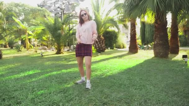 Młody piękna Rudowłosa dziewczyna taniec w parku. Kobieta w mini spódniczkę, taniec w tropikalnym parku na tle Palm. 4k, zwolnionym tempie — Wideo stockowe