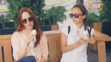 İki genç kadın açık bir kafede oturup dondurma yemek, eğleniyorlar. 4k, ağır çekim, steadicam.