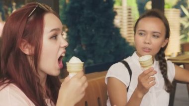 İki genç kadın açık bir kafede oturup dondurma yemek, eğleniyorlar. 4k, ağır çekim, steadicam.