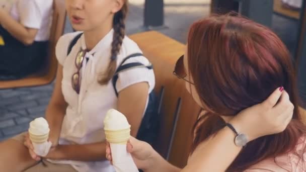 Дві молоді жінки їдять морозиво, сидячи у відкритому кафе, вони розважаються. 4k, повільний рух, стабілізатор . — стокове відео