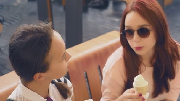Två unga kvinnor äter glass, sitter i ett utomhus café, de har roligt. 4k, ultrarapid, steadicam. — Stockvideo