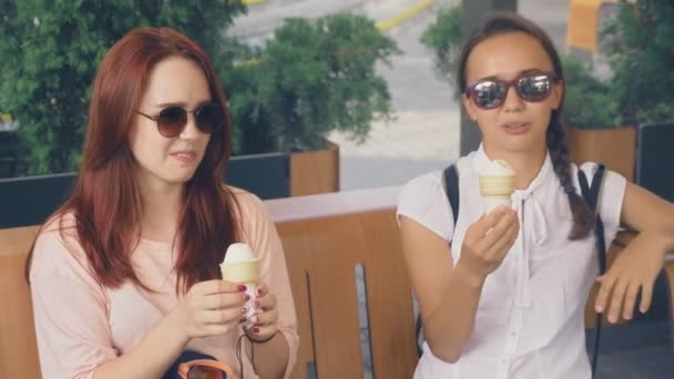 Deux jeunes femmes mangent de la crème glacée, assises dans un café extérieur, elles s'amusent. 4k, ralenti, steadicam . — Video