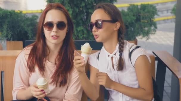 Dos mujeres jóvenes comen helado, se sientan en un café al aire libre, se divierten. 4k, cámara lenta, steadicam . — Vídeo de stock