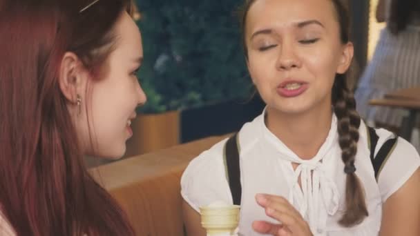 Две молодые женщины едят мороженое, сидя в кафе на открытом воздухе, они веселятся. 4k, slow motion, steadicam . — стоковое видео