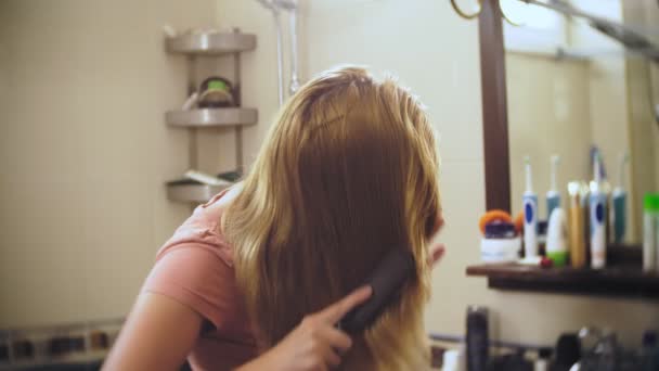 鏡の前で浴室で、長い髪のブロンド女の髪を失う女性をとかし。髪は、櫛に残ります。4 k、スローモーション — ストック動画