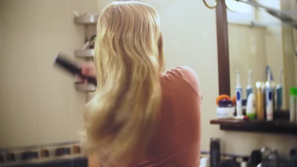 Femme perdant les cheveux, une femme blonde aux cheveux longs est peignée dans la salle de bain devant le miroir. les cheveux restent sur le peigne. 4k, au ralenti — Video