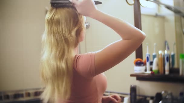 Frau verliert Haare, eine blonde Frau mit langen Haaren wird im Badezimmer vor dem Spiegel gekämmt. Haare bleiben auf dem Kamm. 4k, Zeitlupe — Stockvideo