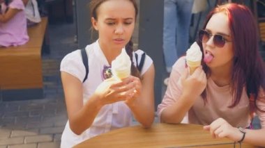 İki genç kadın açık bir kafede oturup dondurma yemek, eğleniyorlar. 4k, ağır çekim, steadicam.