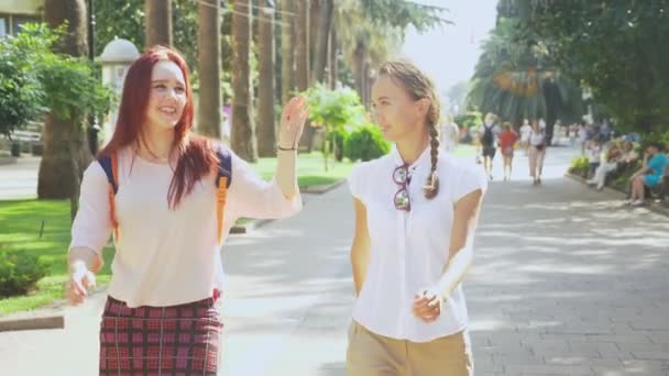 Две девушки, молодые красивые девушки, гуляющие по парку. девушки прогуливаются по курортному городу. Стадикам выстрелил. 4k, slow motion — стоковое видео