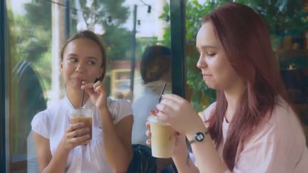 Duas raparigas estão a falar num café ao ar livre. Eles bebem cocktails na rua. 4k, tiro em câmera lenta . — Vídeo de Stock