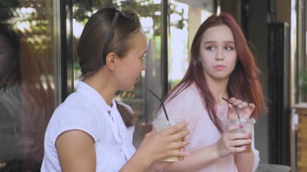 Две девушки разговаривают в кафе на открытом воздухе. Они пьют коктейли на улице. 4к, замедленная съемка . — стоковое видео