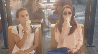 İki genç kadın açık bir kafede oturup dondurma yemek, eğleniyorlar. 4k, ağır çekim, steadicam.