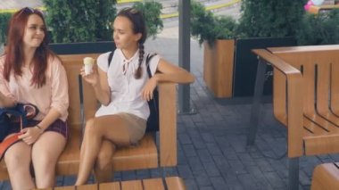 İki genç kadın açık bir kafede oturup dondurma yemek, eğleniyorlar. 4k, ağır çekim, steadicam.