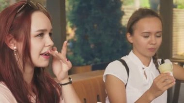 İki genç kadın açık bir kafede oturup dondurma yemek, eğleniyorlar. 4k, ağır çekim, steadicam.