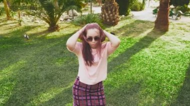 parkta dans genç güzel kızıl saçlı kız. tropikal bir parkta avuç içi bir arka plan üzerinde dans mini etek kadında. 4k, ağır çekim