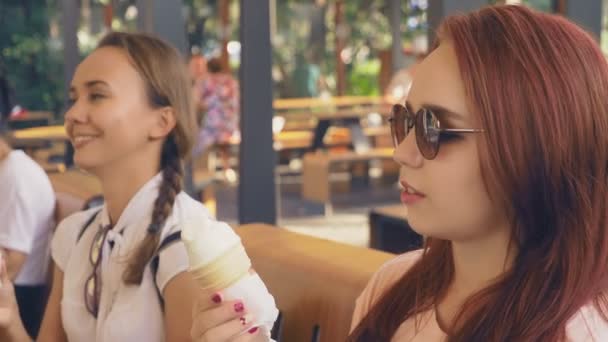 Δύο νεαρές γυναίκες τρώνε παγωτό, κάθεται σε μια υπαίθρια καφετέρια, έχουν διασκέδαση. 4k, αργή κίνηση, steadicam. — Αρχείο Βίντεο