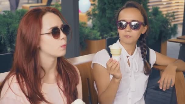 Две молодые женщины едят мороженое, сидя в кафе на открытом воздухе, они веселятся. 4k, slow motion, steadicam . — стоковое видео